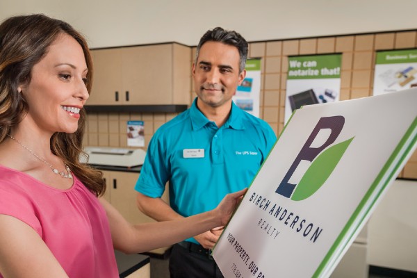 A person holding a sign with a UPS store employee beside them.